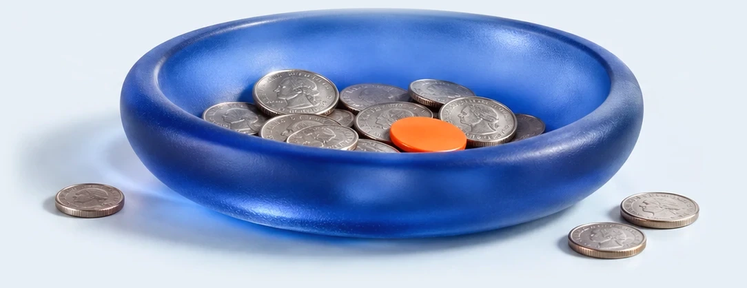 A low, wide dish of frosted cobalt glass holding a handful of silver coins and one small orange disc. A few coins rest on the surface beside it.